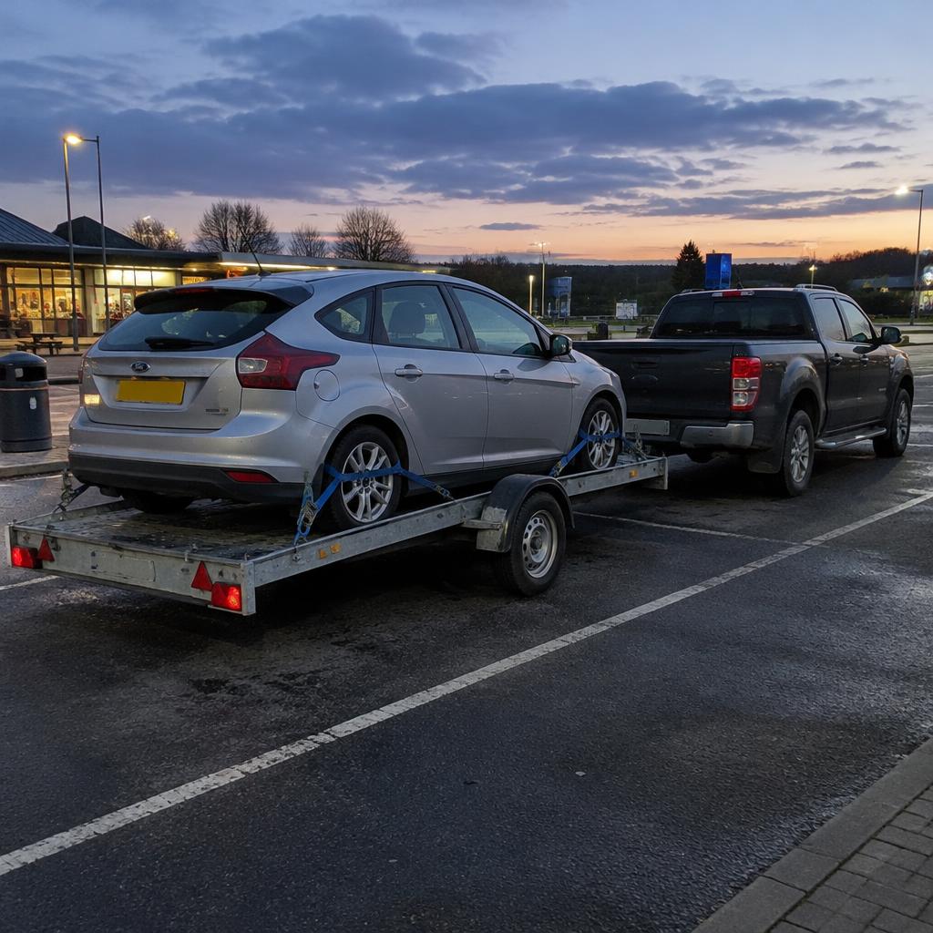 Silver car strapped to a single trailer at motorway services